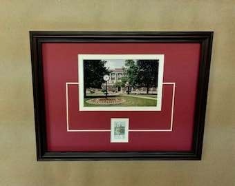 May include: A framed photograph of a building with a clock tower. The photo is matted with a white mat and a red mat. A smaller stamp is also framed below the photo.