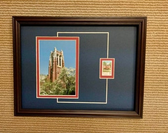 May include: A framed photograph of a brick building with a tall tower. The building is surrounded by trees with white flowers. A smaller framed photograph of the same building is in the bottom right corner of the frame.