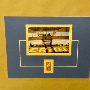 May include: A framed photograph of a vintage airplane with a yellow mat and a blue background. The airplane is on a runway with the word "ERAU" visible. A small postage stamp with a picture of an airplane is in the lower right corner.