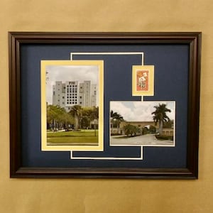 May include: Framed collage featuring three images: a building with "FIU" text, a stamp, and a road with an archway. The collage is set against a dark blue background within a brown wooden frame. The images are in cream-colored mats.