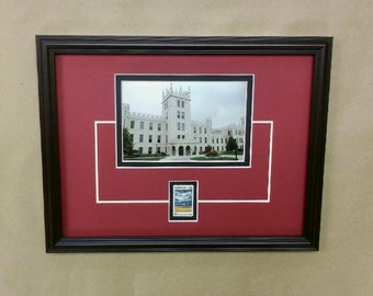 May include: A framed photograph of a white building with a red mat and a white border. The building has a tall tower and a clock on the front. The photo is surrounded by a black frame. A small stamp is in the lower center of the mat.