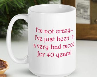 May include: White ceramic mug with a large handle. The mug features the text "I'm not crazy... I've just been in a very bad mood for 40 years!" in pink lettering. The mug is a humorous gift idea.