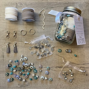Può includere: Un barattolo di vetro pieno di varie perline, ciondoli e cordini per la creazione di gioielli. Il barattolo è etichettato "Charming Crafty Things" e "Collezione di creazione di gioielli".