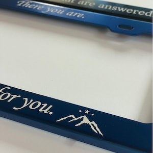 Peut inclure: Cadre de plaque d'immatriculation en m&eacute;tal bleu avec le texte "There you are. For you." et un motif de montagnes blanches avec des &eacute;toiles.