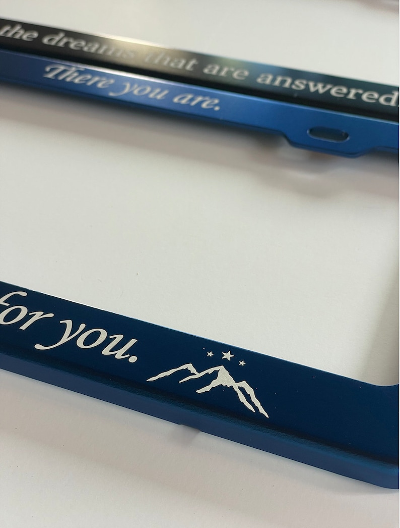 Peut inclure: Cadre de plaque d'immatriculation en m&eacute;tal bleu avec le texte "There you are. For you." et un motif de montagnes blanches avec des &eacute;toiles.