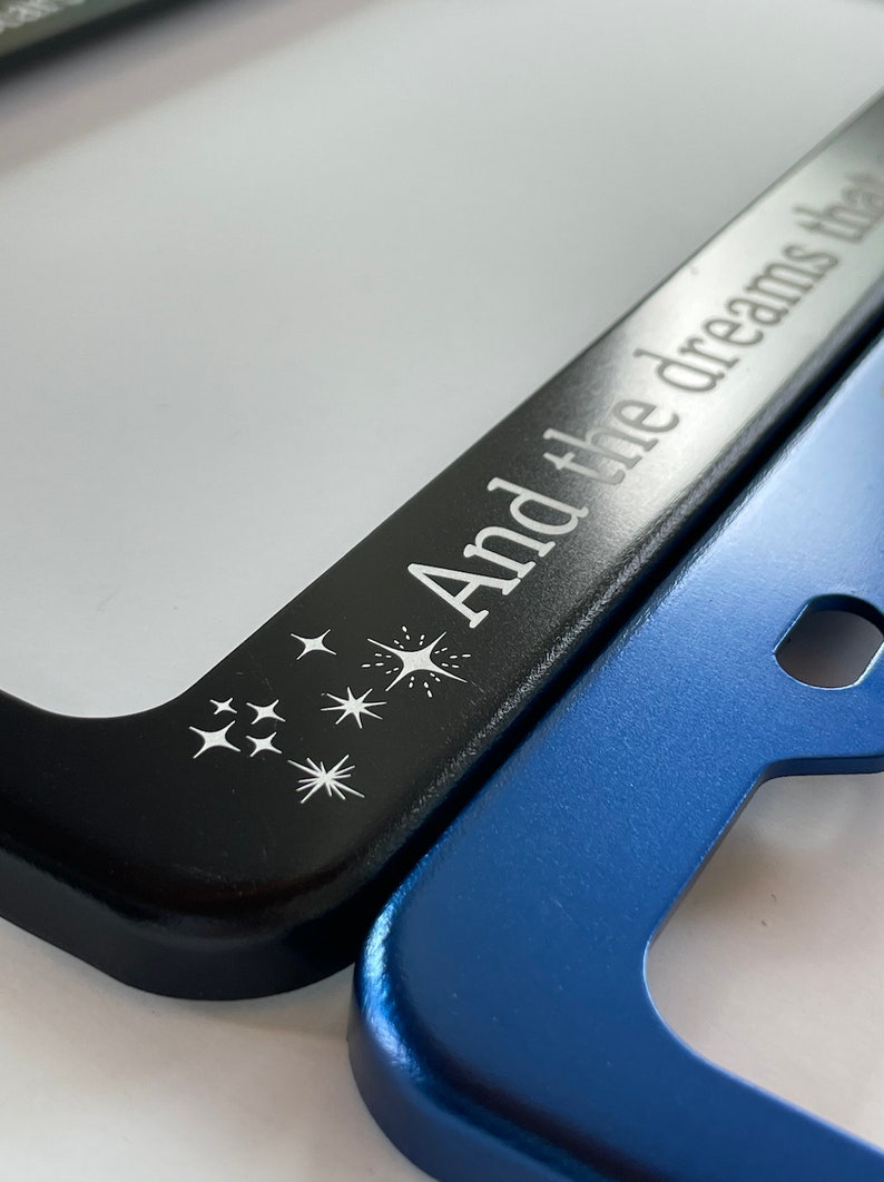 Peut inclure: Cadre de plaque d'immatriculation noir avec le texte "And the dreams they" et un motif d'&eacute;toiles blanches. Le cadre recouvre partiellement un cadre de plaque d'immatriculation bleu.