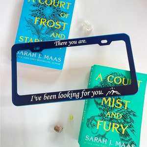 Peut inclure: Un cadre de plaque d'immatriculation bleu avec le texte "There you are." et "I've been looking for you." avec un graphique de montagne. Le cadre est &agrave; c&ocirc;t&eacute; de deux livres avec des couvertures bleu sarcelle pr&eacute;sentant un motif floral et le texte "A Court of Frost and Starlight" et "A Court of Mist and Fury" de Sarah J. Maas.
