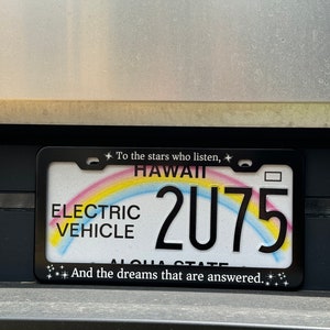 Peut inclure: Cadre de plaque d'immatriculation noir avec un motif arc-en-ciel et le texte "To the stars who listen, Hawaii 2075 And the dreams that are answered."