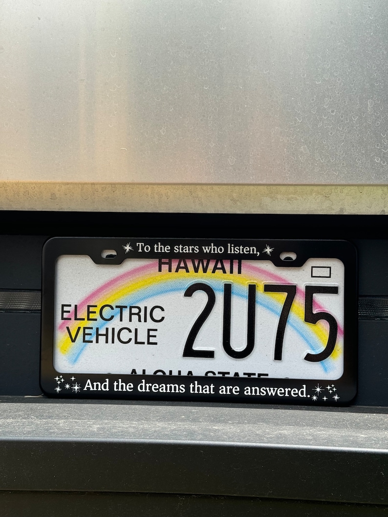 Peut inclure: Cadre de plaque d'immatriculation noir avec un motif arc-en-ciel et le texte "To the stars who listen, Hawaii 2075 And the dreams that are answered."