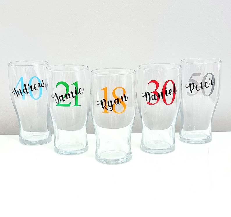 Puede incluir: Cinco vasos de pinta de vidrio transparente con nombres y n&uacute;meros personalizados. Los nombres son Andrew, Jamie, Ryan, Daniel y Peter. Los n&uacute;meros son 40, 21, 18, 30 y 50. Los n&uacute;meros son de diferentes colores.