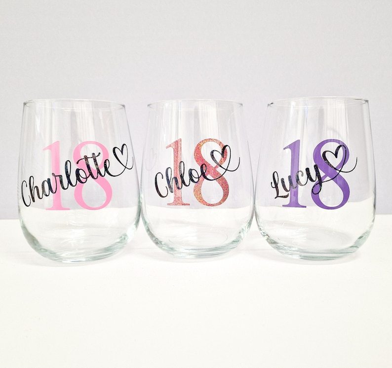 May include: Three clear stemless wine glasses with custom text. Each glass has the number "18" in a different color, with a name and heart design. The names are "Charlotte", "Chloe", and "Lucy".