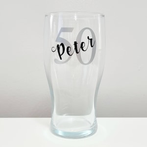 Puede incluir: Un vaso de pinta de vidrio transparente con una pegatina de vinilo negro que dice "Peter 50".