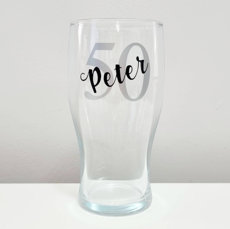 Puede incluir: Un vaso de pinta de vidrio transparente con una pegatina de vinilo negro que dice "Peter 50".