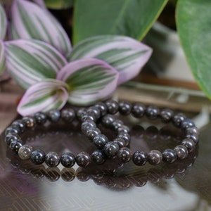 Peut inclure: Deux bracelets en perles noires avec un motif moucheté, posés sur une surface à motifs.