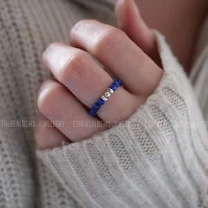 Op de afbeelding: Een zilveren ring met blauwe edelsteen kralen. De ring zit aan een vinger.
