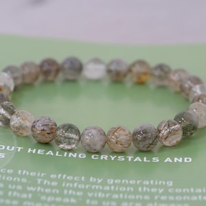 May include: A bracelet made of clear quartz beads with inclusions of black and gold. The beads are round and have a smooth, polished finish.