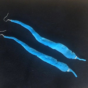 Può includere: Un paio di lunghi orecchini blu e pelosi con ganci d'argento. Gli orecchini hanno la forma di vermi.