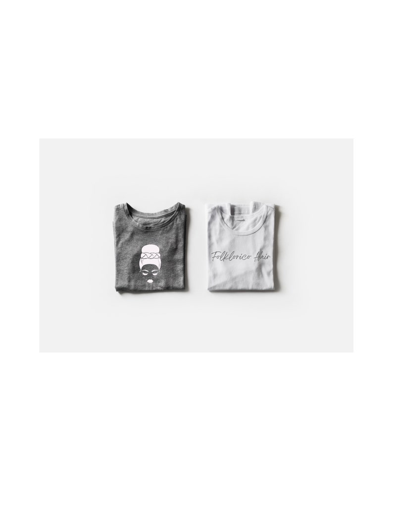May include: Two folded t-shirts, one gray and one white. The gray t-shirt has a white graphic of a woman with a bun and the text "Folklorico Hair". The white t-shirt has the text "Folklorico Hair" in black.