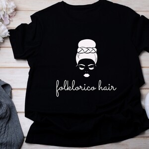 May include: Black t-shirt with a white graphic of a woman with a bun and the text "folklorico hair".