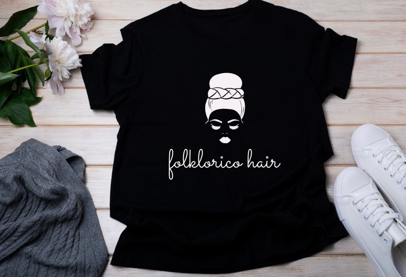 May include: Black t-shirt with a white graphic of a woman with a bun and the text "folklorico hair".