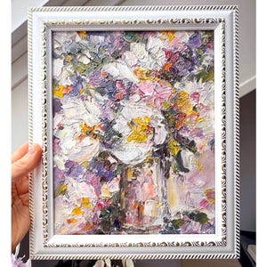 May include: A framed floral oil painting featuring a bouquet of white, pink, yellow, and purple flowers. The artwork is in a white ornate frame. The painting has a textured, impasto style, with visible brushstrokes.