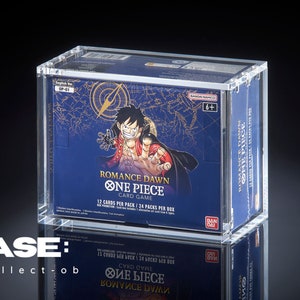 Puede incluir: Una vitrina transparente de acrílico que contiene una caja de "Romance Dawn One Piece Card Game". La caja es azul con detalles dorados y presenta una ilustración de personaje. La vitrina está etiquetada "CASE: by-collect-ob".