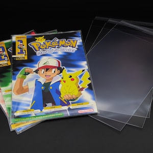 Puede incluir: Cuatro revistas de Pokemon de colores con una portada azul que presenta a Pikachu y Ash Ketchum. Las revistas están apiladas una encima de la otra y están protegidas por fundas de plástico transparentes.