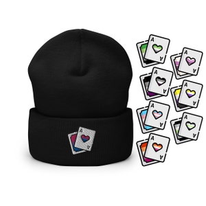 May include: Black beanie with a white ace of hearts playing card design featuring a pink and blue heart. The card is surrounded by a rainbow colored border.