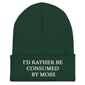 May include: A dark green beanie with the text "I'd rather be consumed by moss" embroidered in white.