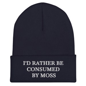 May include: Navy blue beanie with white embroidered text that reads "I'd rather be consumed by moss".