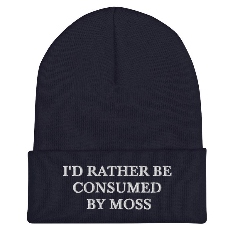 May include: Navy blue beanie with white embroidered text that reads "I'd rather be consumed by moss".
