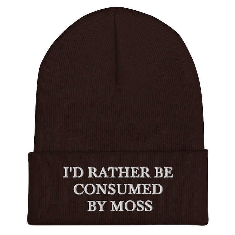 May include: A brown knit beanie with the text "I'd rather be consumed by moss" embroidered in white on the front.