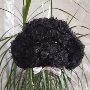 May include: Black fluffy poodle ornament with a white bow. The ornament is made of fabric and has a shiny black nose and eyes.