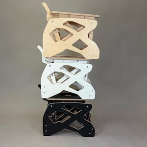 Puede incluir: Una pila de tres sillas de madera para ni&ntilde;os en colores natural, blanco y negro. Cada silla tiene un dise&ntilde;o recortado &uacute;nico y un respaldo curvo. Las sillas est&aacute;n hechas de madera y ensambladas con tornillos.