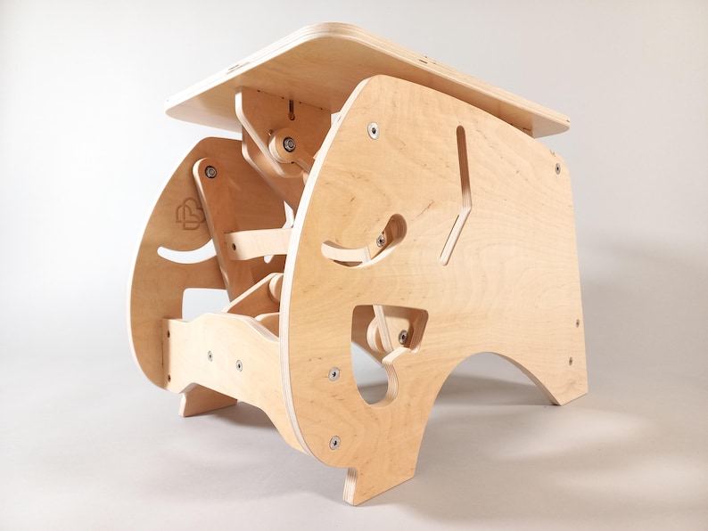 Puede incluir: Un escritorio de pie ajustable de madera de color claro. El escritorio tiene una parte superior rectangular y una base compleja y dise&ntilde;ada con formas recortadas y herrajes visibles. El escritorio est&aacute; dise&ntilde;ado para ser ajustable para uso ergon&oacute;mico.