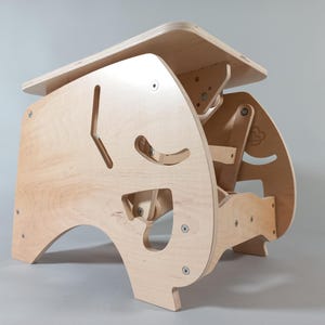 Puede incluir: Un escritorio infantil de madera clara con un dise&ntilde;o geom&eacute;trico &uacute;nico. El escritorio presenta formas recortadas y una peque&ntilde;a mesa rectangular. El escritorio est&aacute; hecho de madera contrachapada y tiene tornillos visibles.