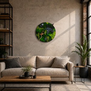 May include: A circular wall art piece featuring a collection of preserved green moss, dark fern leaves, and a light-colored wooden branch element. The arrangement is contained within a thin, dark circular frame, creating a textured botanical display.