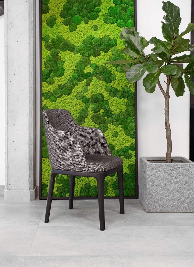 Op de afbeelding: Een donkergrijze gestoffeerde fauteuil met een textuurrijke stoffen afwerking en donkerhouten poten. De stoel heeft een gebogen rugleuning en ge&iuml;ntegreerde armleuningen, wat zorgt voor een gestructureerde zithouding. Hij staat voor een groot rechthoekig wandpaneel bedekt met felgroen geconserveerd mos.