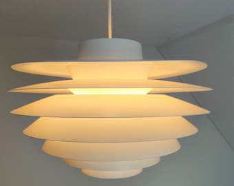Puede incluir: Una lámpara colgante blanca de varios niveles con un diseño moderno. La luz está encendida y emite un brillo cálido amarillo.
