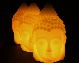 May include: Four illuminated Buddha head sculptures in a row, glowing with a warm orange light against a black background. The sculptures have closed eyes and detailed hair, creating a serene and spiritual ambiance.