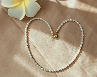 May include: A white pearl necklace with a gold clasp, arranged in a heart shape on a light brown fabric background.