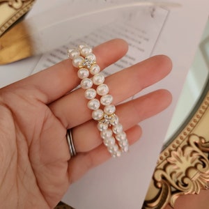 May include: A double strand pearl bracelet with a gold clasp and a small diamond accent.