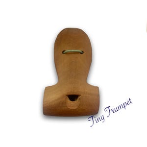 Puede incluir: Una trompeta de juguete de madera con un acabado marrón claro. La trompeta tiene un pequeño agujero para soplar y una cuerda atada alrededor de la parte superior.