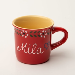 Könnte beinhalten: Rote Keramiktasse mit gelbem Innenraum und einem weißen Blumendesign am Rand. Die Tasse hat einen roten Henkel und den Namen "Mila" in weiß mit einem blauen Herzen geschrieben.