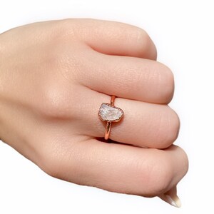 Könnte beinhalten: Ein Ring aus Roségold mit einem klaren, rohen Edelstein. Der Ring wird an einem Finger getragen.