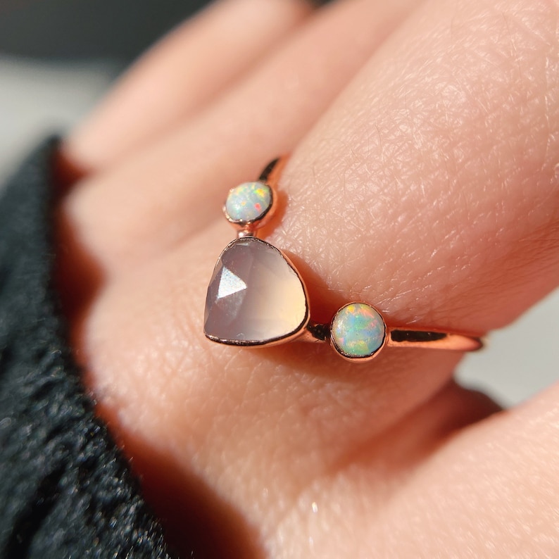May include: A rose gold ring with a heart-shaped chalcedony gemstone and two smaller opal gemstones.