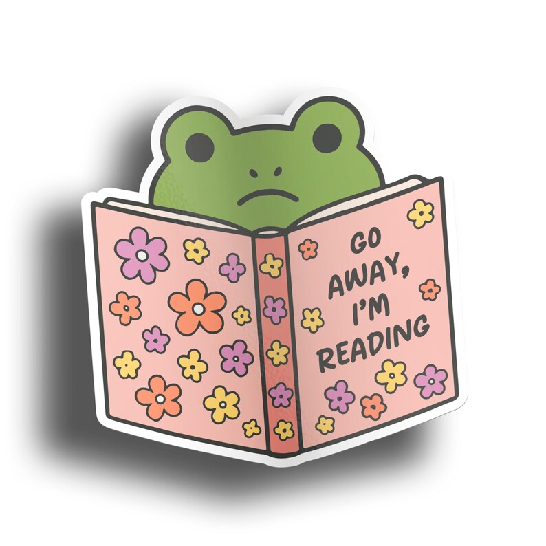May include: A sticker featuring a green frog peeking over a pink book. The book is decorated with colorful flowers and the text "GO AWAY, I'M READING". The frog has a sad expression.