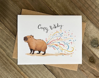 May include: A white card with a cartoon capybara with a stream of colorful confetti coming out of its rear end. The card says "Capy Birthday" in black cursive writing.