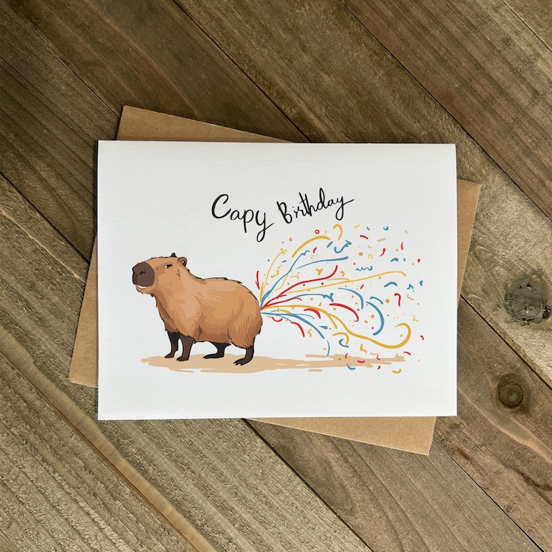 May include: A white card with a cartoon capybara with a stream of colorful confetti coming out of its rear end. The card says "Capy Birthday" in black cursive writing.