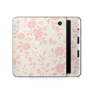 May include: A rectangular electronic e-reader device featuring a cream-colored skin with a repeating pattern of soft pink roses, buds, and leaves. The device has a black side panel with visible buttons and a camera lens located on the top corner.